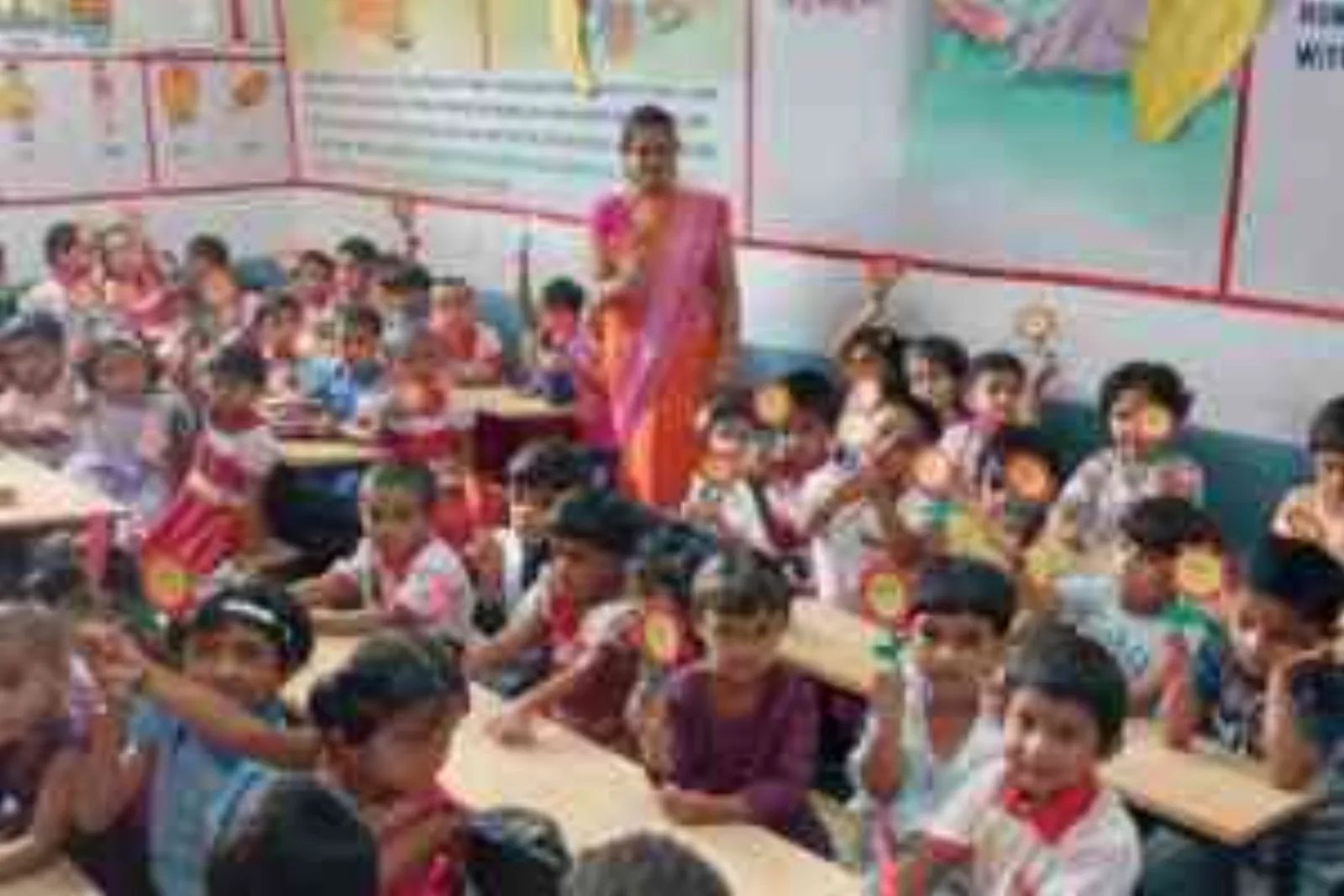 Nursery children seated at their desks in a colourfully decorated classroom with a teacher