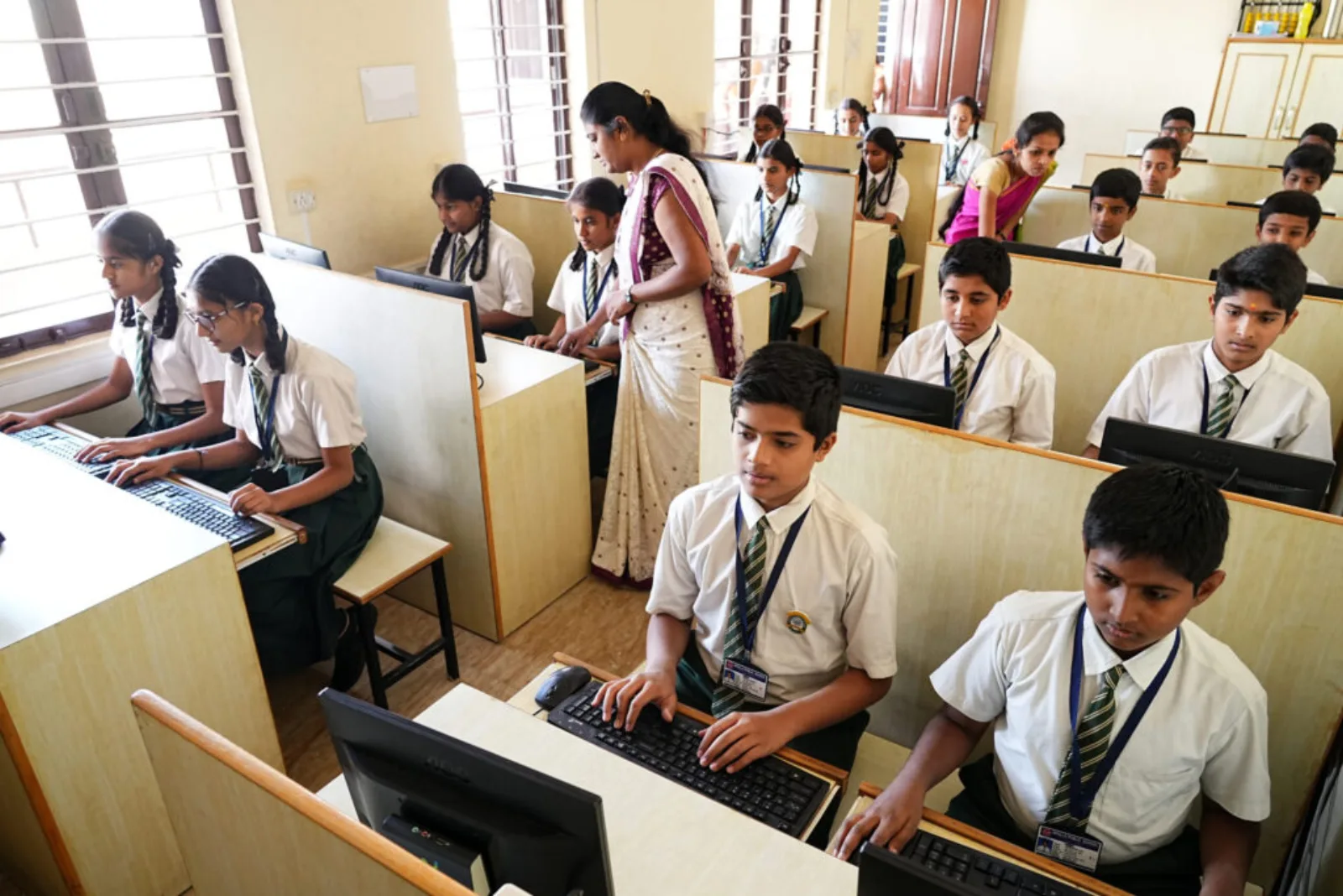 Primary students working at computers in the computer lab with a teacher supervising