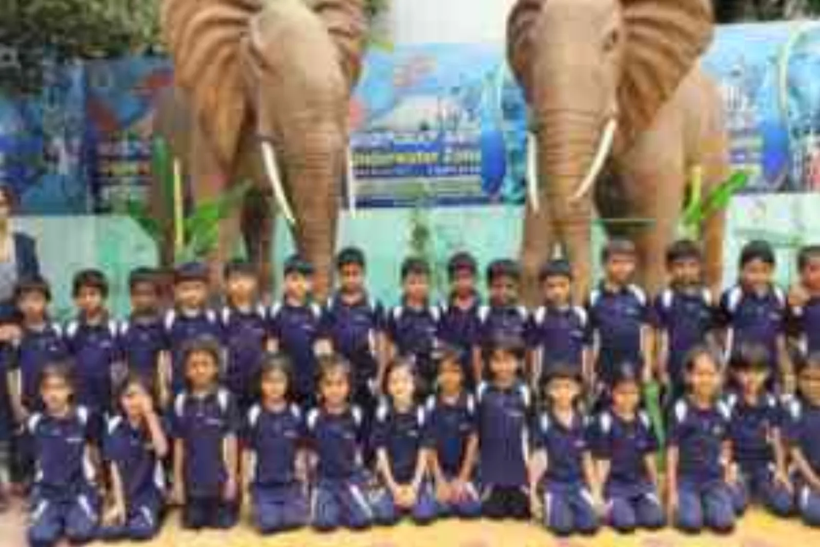 Primary students in navy blazers posing together in front of large elephant statues on a field trip
