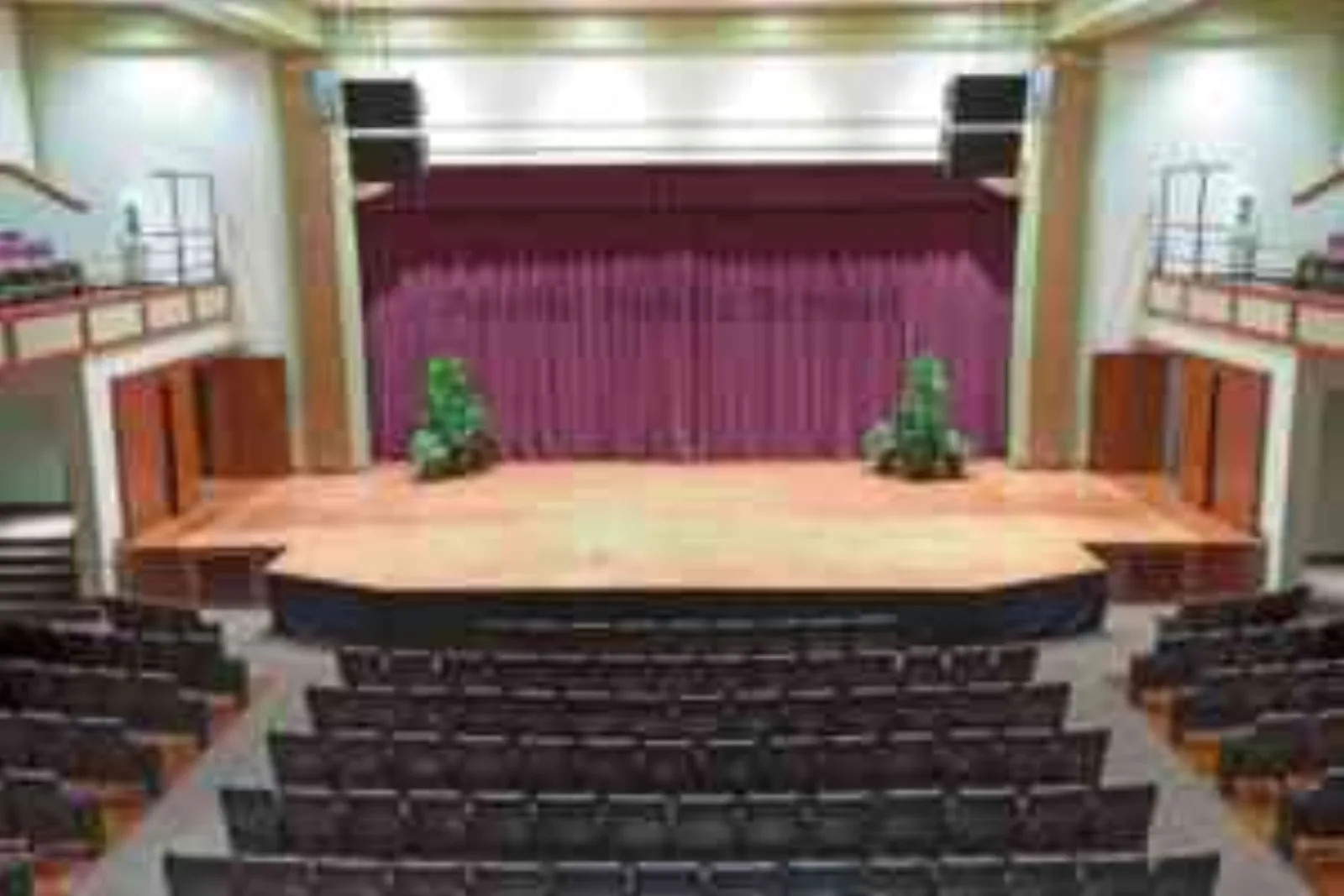 An empty auditorium with rows of red seats facing a curtained stage