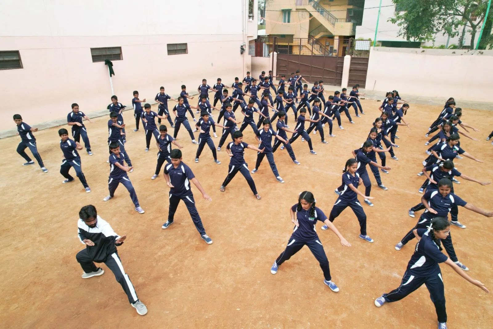Students in tracksuits performing a physical training formation on the school ground