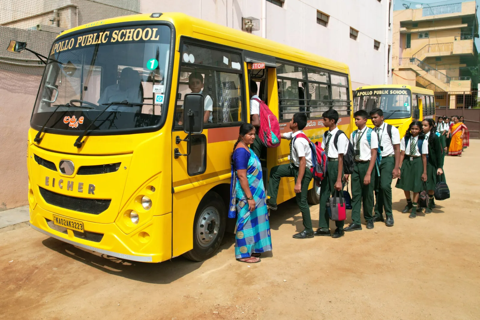A yellow school bus parked outside the school with staff and students boarding