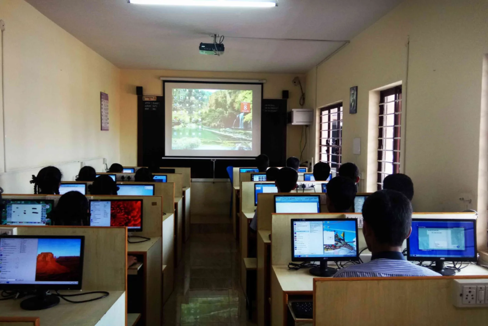 A smart classroom with a large projector screen and rows of computer monitors