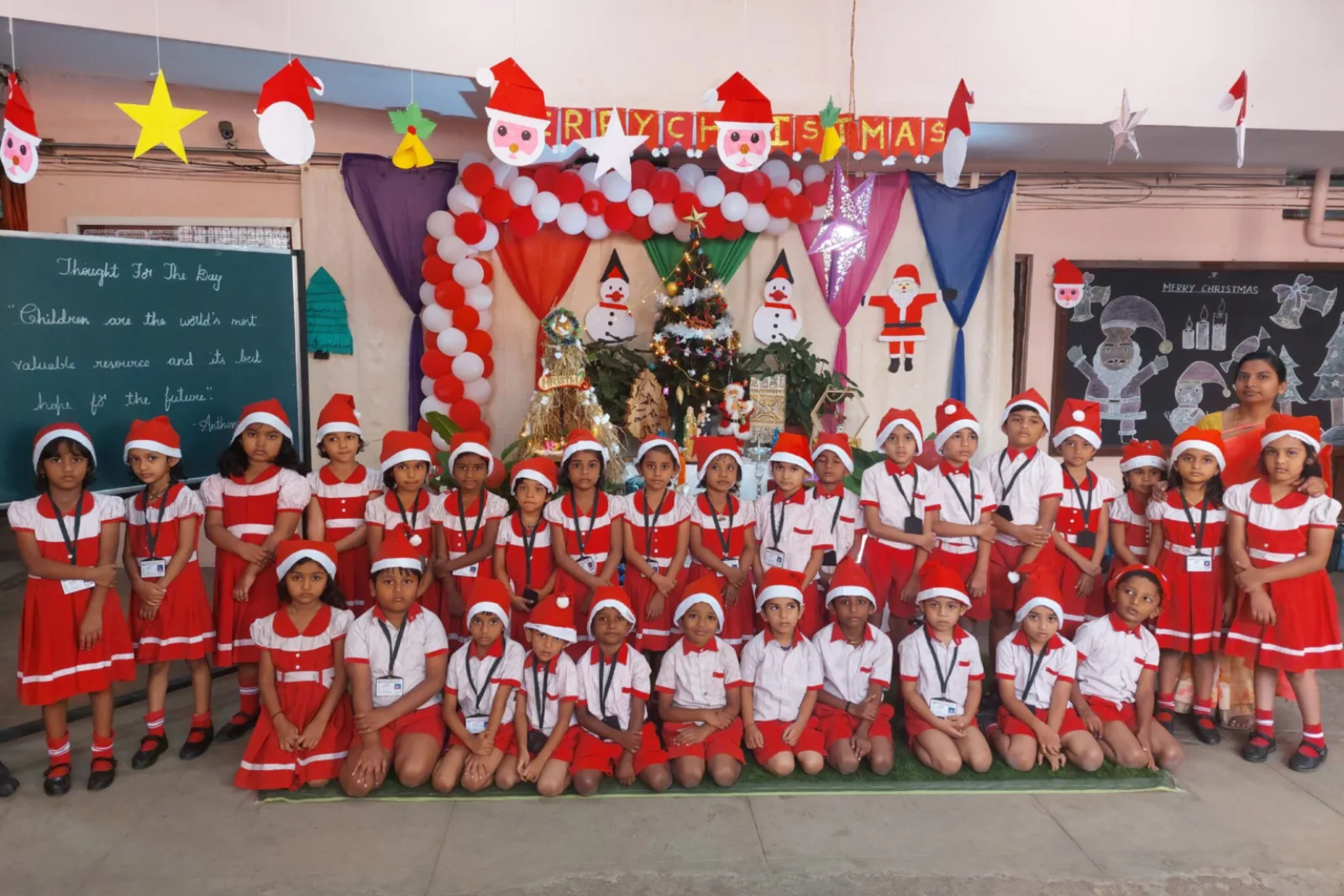 Children dressed in red and white Christmas outfits celebrating in a decorated classroom