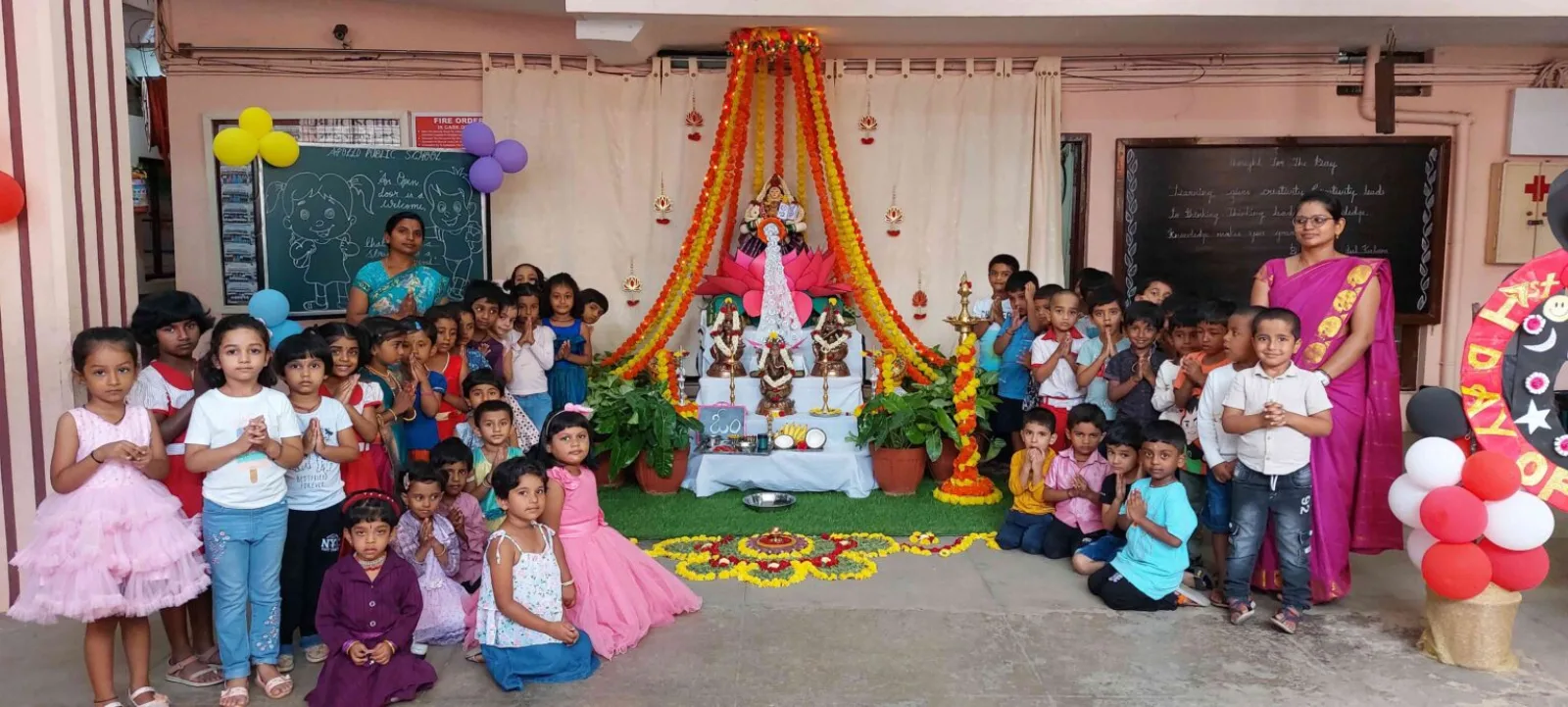 Children sitting together on the floor for a festive school celebration in a decorated corner of a classroom