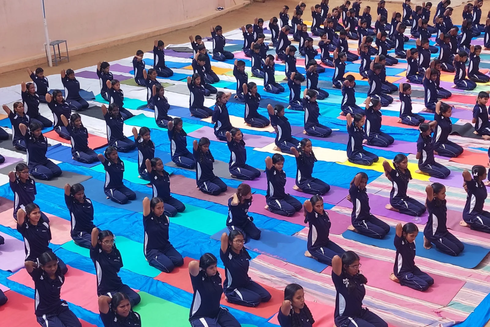 Hundreds of students performing a coordinated yoga display on mats laid out across the ground