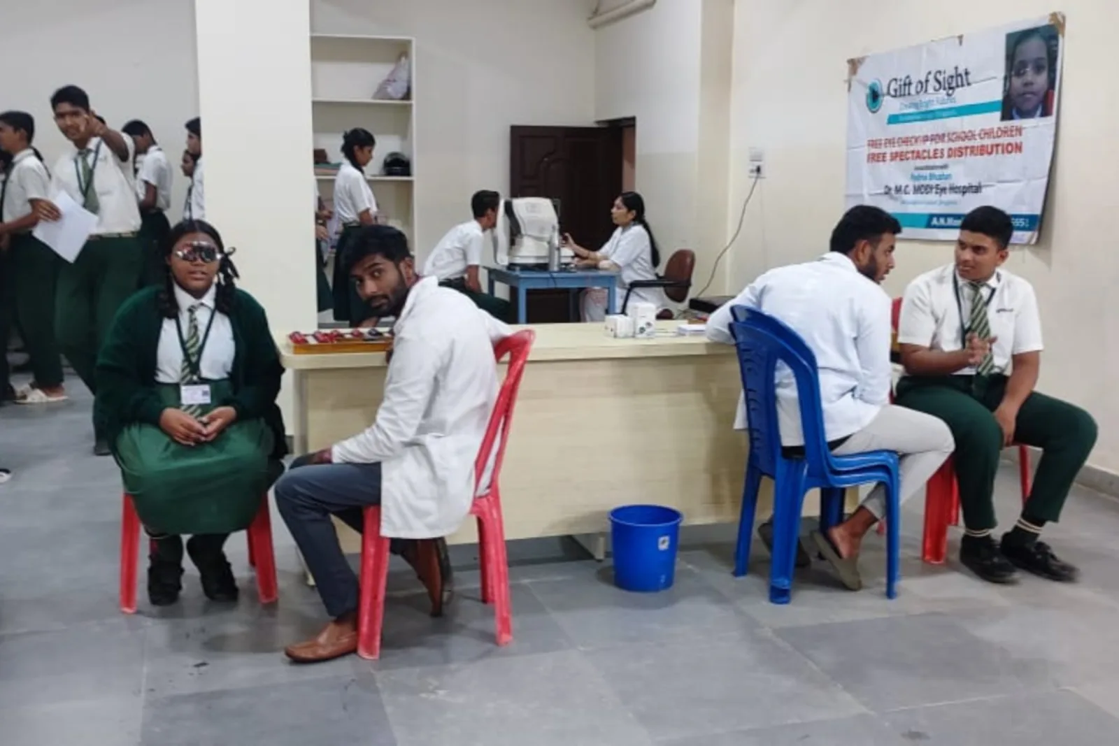 A doctor administering a vaccination to a young student as other children and staff look on